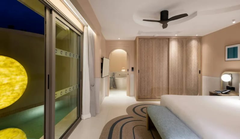 Three Bedroom Pool Villa warm indoor lighting, a king bed, and sliding glass doors revealing an illuminated private pool area with glowing wall art at Centara Karon Villas Phuket by Kenwood Travel