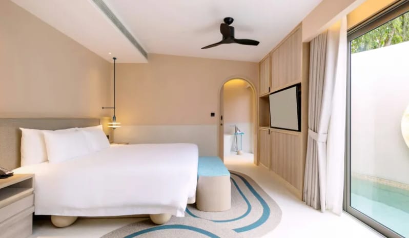 Three Bedroom Pool Villa Bright 3-bedroom villa bedroom showing a king-size bed, teal bed bench, large wardrobe, and an arched entryway leading to a private bathtub at Centara Karon Villas Phuket by Kenwood Travel