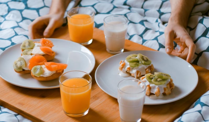 In-room Dining Luxury room service breakfast in bed with fresh orange juice, milk, and fruit-topped waffles served on a wooden tray at Centara Karon Villas Phuket by Kenwood Travel