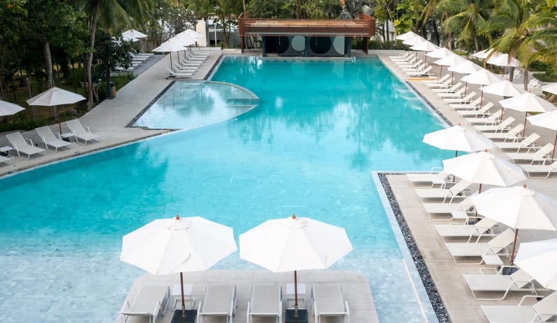Tropix  Luxury outdoor swimming pool at CKR tropical resort lined with white lounge chairs and umbrellas at Centara Karon Villas Phuket by Kenwood Travel