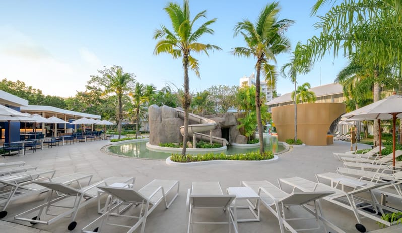 Koh Kool Large lagoon-style swimming pool at a luxury tropical resort featuring a rock water slide, palm trees, and white lounge chairs at Centara Karon Villas Phuket by Kenwood Travel