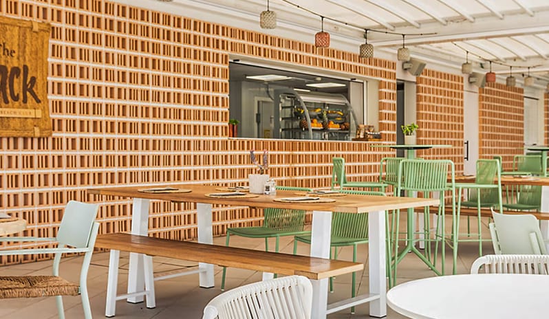 The Shack - Snack Bar & Restaurant light green and white modern chairs, wooden dining tables, and a textured brick bar area with hanging woven lights at Paradisus Gran Canaria by Kenwood Travel