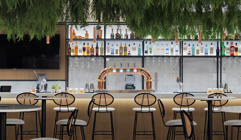 Vibra-Fun Bar & Restaurant Modern bar interior with a white marble counter, copper beer taps, and lush green ferns hanging from the ceiling at Paradisus Gran Canaria by Kenwood Travel