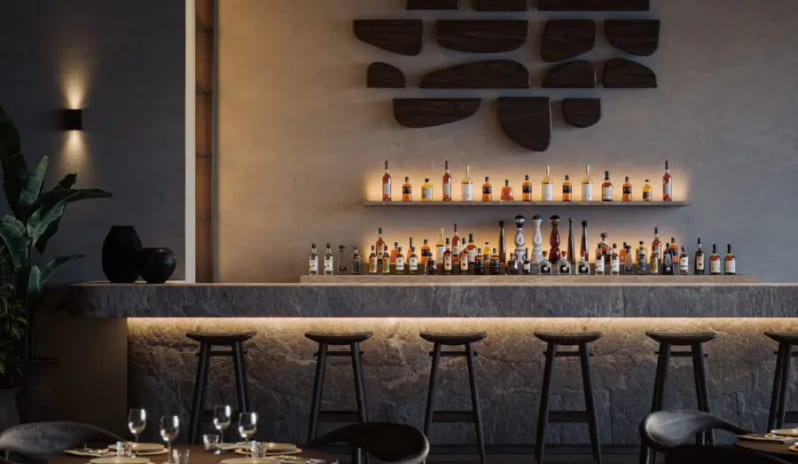 To Kima Modern luxury bar with a textured stone counter, backlit liquor shelves, and dark wooden wall art in a moody restaurant setting. at OKU Bodrum by Kenwood Travel