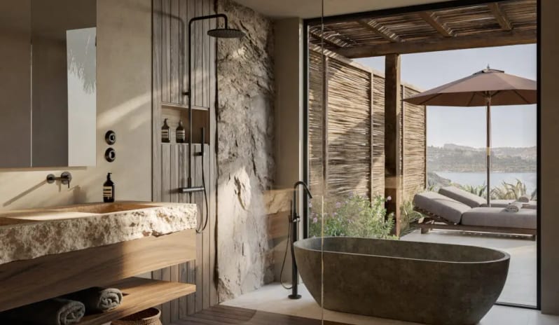 OKU Signature Suite with Private Pool organic modern bathroom featuring a freestanding stone bathtub, a raw-edge stone vanity, and floor-to-ceiling glass walls overlooking a Mediterranean terrace with a sea view at OKU Bodrum by Kenwood Travel