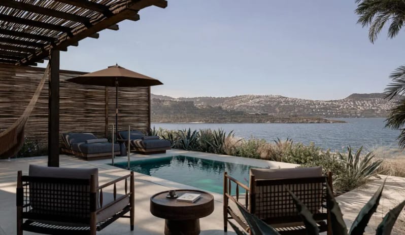 Two Bedroom Suite with Private Pool Luxury villa patio with a private plunge pool, wooden lounge chairs, and a large umbrella overlooking a calm blue sea and coastal hills at OKU Bodrum by Kenwood Travel