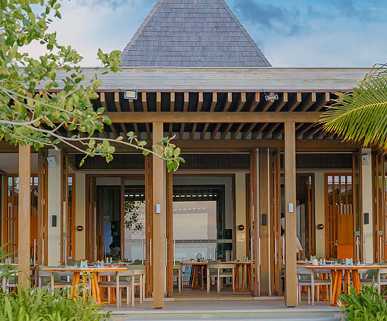 Earth Exterior view of a luxury tropical restaurant on a white sand beach, featuring a modern pyramid-style shingle roof, wooden pillars, and open-air dining at Kuda Villingili Resort Maldives by Kenwood Travel