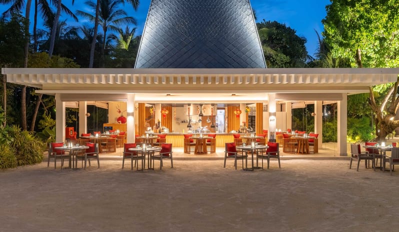 East Luxury tropical resort dining area with outdoor tables, palm trees, and an open kitchen layout during the evening blue hour at Kuda Villingili Resort Maldives by Kenwood Travel