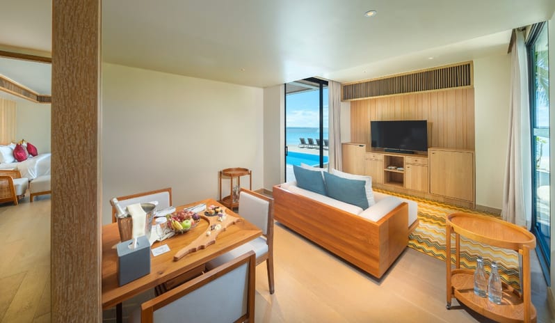 Two Bedroom Beach Residence with Private Pool luxury beach suite living room featuring a wooden dining set with a fruit platter, a contemporary lounge area with a flat-screen TV, and sliding glass doors opening to a private pool and ocean views at Kuda Villingili Resort Maldives by Kenwood Travel
