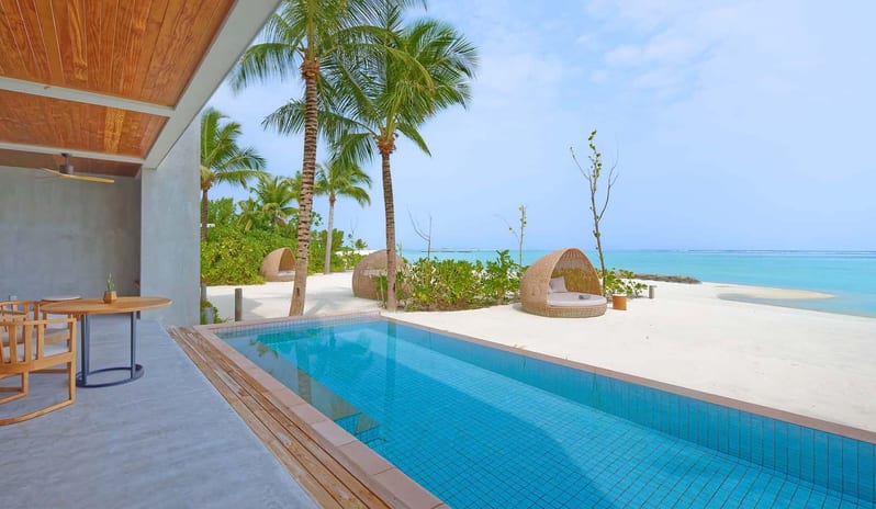 Two Bedroom Beach Residence with Private Pool private lap pool, wooden dining furniture, and woven sun pods on a white sand beach under palm trees at Kuda Villingili Resort Maldives by Kenwood Travel