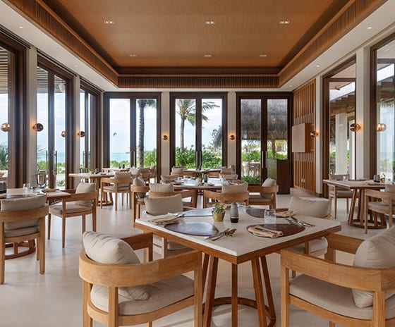 Earth Close-up of a luxury restaurant interior featuring square marble-top tables, handcrafted wooden chairs, and a textured tray ceiling with recessed lighting at Kuda Villingili Resort Maldives by Kenwood Travel