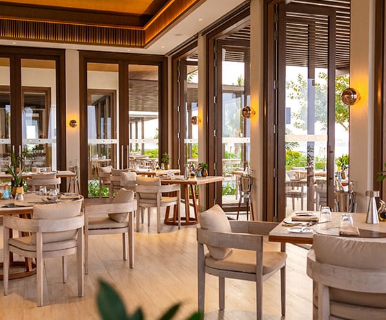 Fire Contemporary beachfront bistro interior showing circular wooden tables, minimalist wall sconces, and polished light wood flooring at Kuda Villingili Resort Maldives by Kenwood Travel