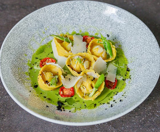 Med Handmade yellow tortellini pasta served on a bright green pesto base with shaved parmesan cheese, sun-dried tomatoes, and fresh asparagus in a textured bowlat Kuda Villingili Resort Maldives by Kenwood Travel