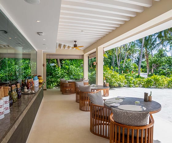 Spice Modern wooden seating at The Spice restaurant in Atmosphere Kanifushi Maldives, showing the covered terrace overlooking tropical greenery at Kuda Villingili Resort Maldives by Kenwood Travel