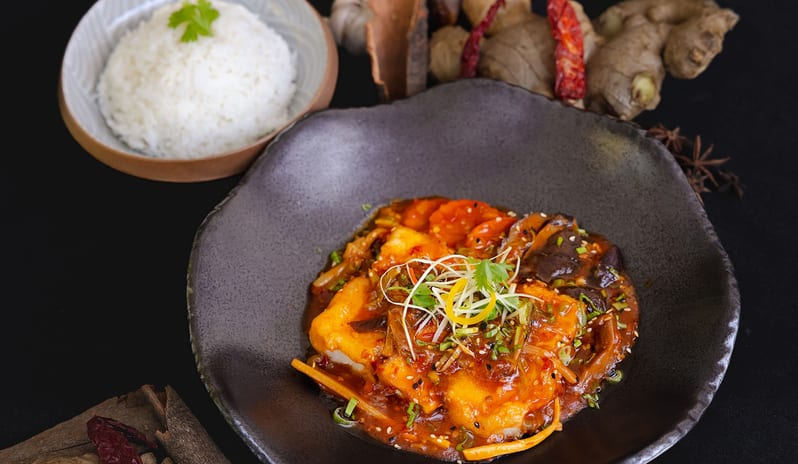 East beautifully plated Asian stir-fry dish with golden tofu, glazed vegetables, and sesame seeds in a dark ceramic bowl, served with a side of fluffy white steamed riceat Kuda Villingili Resort Maldives by Kenwood Travel