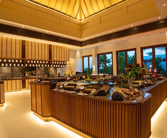 The Restaurant Maldivian Night theme with warm ambient lighting, wood-paneled food stations, and a high vaulted ceiling with traditional architectural details at Kuda Villingili Resort Maldives by Kenwood Travel