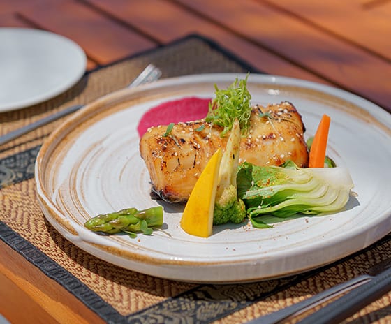 Mar-Umi A perfectly seared white fish fillet glazed with honey or miso, served with bok choy, asparagus, and baby carrots on a textured ceramic plate at Kuda Villingili Resort Maldives by Kenwood Travel