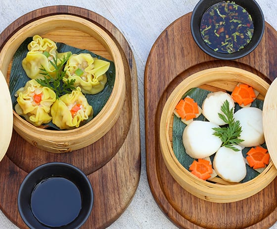 East Freshly steamed artisanal Dim Sum including prawn and pork dumplings garnished with carrots and herbs, presented in traditional bamboo baskets at Kuda Villingili Resort Maldives by Kenwood Travel