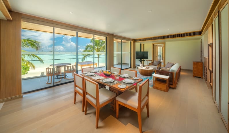 Three bedroom Beach Residence with Private Pool set table for six, hardwood floors, and sliding glass doors revealing a white sand beach and turquoise ocean at Kuda Villingili Resort Maldives by Kenwood Travel
