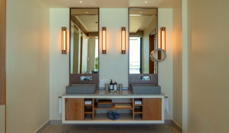 Three bedroom Beach Residence with Private Pool two grey stone vessel sinks, tall rectangular mirrors with warm sconce lighting, and a floating wooden cabinet at Kuda Villingili Resort Maldives by Kenwood Travel