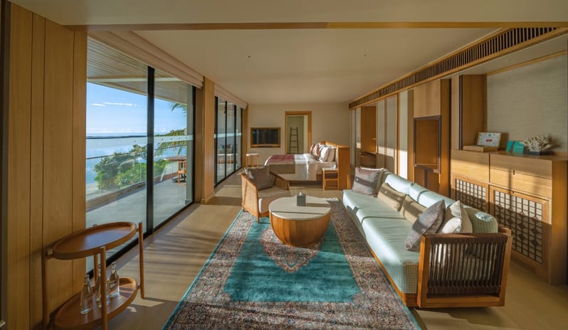 Three bedroom Beach Residence with Private Pool modern bedroom and living area with wood paneling, a blue patterned rug, and floor-to-ceiling glass doors opening to a tropical garden at Kuda Villingili Resort Maldives by Kenwood Travel