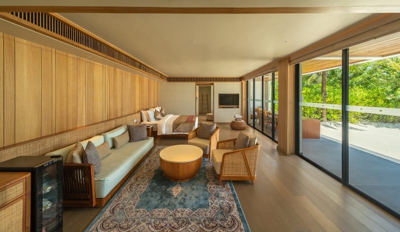 Three bedroom Beach Residence with Private Pool modern bedroom and living area with wood paneling, a blue patterned rug, and floor-to-ceiling glass doors opening to a tropical garden at Kuda Villingili Resort Maldives by Kenwood Travel