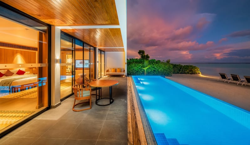 Two Bedroom Beach Residence with Private Poolilluminated private lap pool, a wooden deck with seating, and a vibrant purple sunset over the ocean at Kuda Villingili Resort Maldives by Kenwood Travel