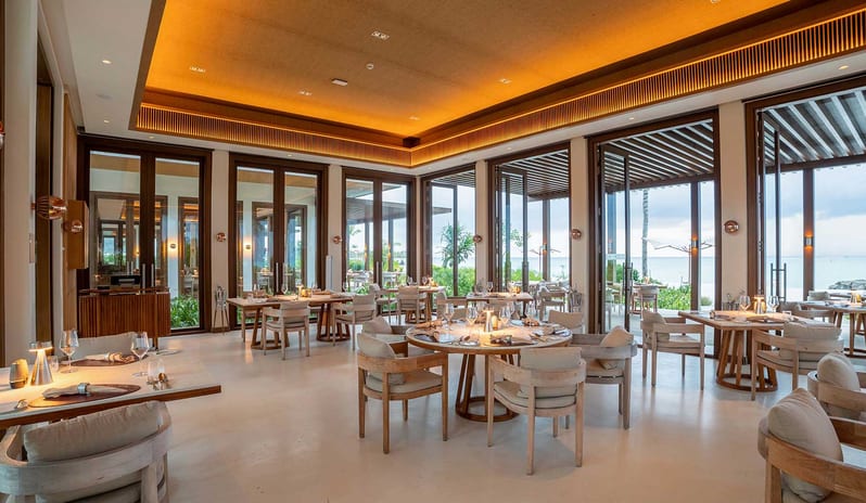 Earth Modern tropical resort restaurant featuring circular wooden tables, plush seating, and an open-air architectural design with a sea view at Kuda Villingili Resort Maldives by Kenwood Travel