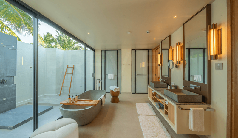 Sunrise Beach Villa with Private Pool bathroom featuring a freestanding stone bathtub, double vanity with stone sinks, and large glass doors opening to a private outdoor shower area at Kuda Villingili Resort Maldives by Kenwood Travel