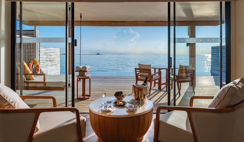 Sunrise Water Villa with Private Pool Private terrace of a luxury overwater villa featuring an infinity pool, outdoor seating, and a champagne setup on a wooden coffee table with a panoramic sea view at Kuda Villingili Resort Maldives by Kenwood Travel