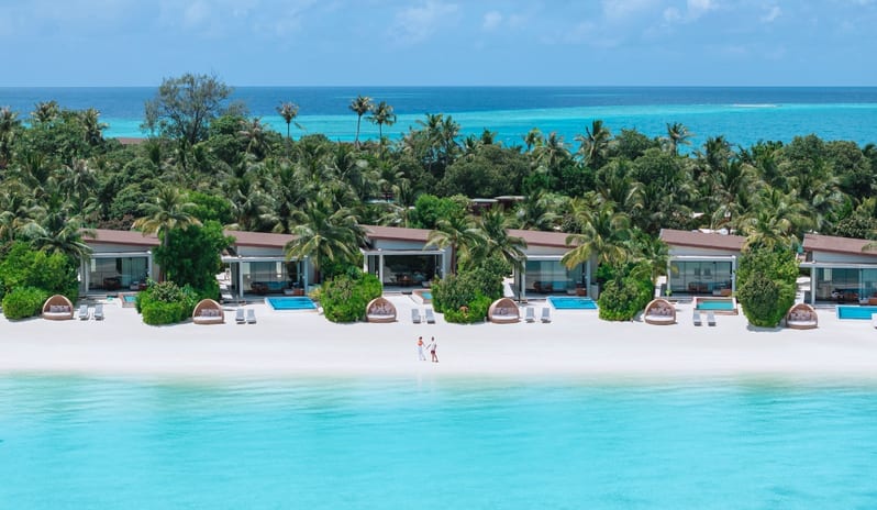 Sunset Water Villa with Private Pool luxury beach villas nestled in lush palm trees along a white sand beach, featuring private turquoise plunge pools and woven daybeds overlooking the ocean at Kuda Villingili Resort Maldives by Kenwood Travel