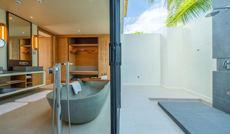 Sunset Beach Villa with Private Pool bathroom featuring a freestanding stone bathtub, double vanity with integrated lighting, and a walk-in closet adjacent to a private semi-outdoor rainfall shower area at Kuda Villingili Resort Maldives by Kenwood Travel