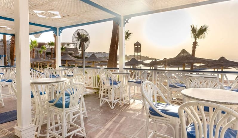 White Knight Sunlit outdoor patio bar at a luxury beach resort with white wicker chairs overlooking the ocean during sunset at Royal Savoy Sharm El Sheikh by Kenwood Travel