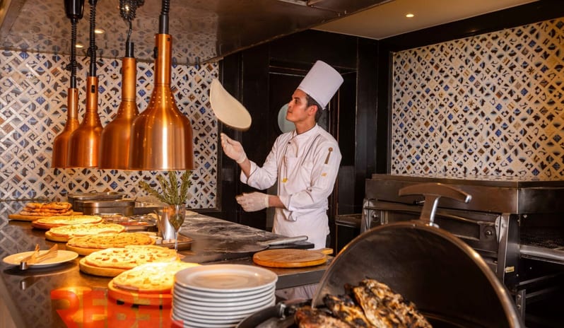 TiranaA live cooking station at a resort restaurant where a chef tosses fresh dough next to a display of cooked pizzas and grilled food counters at Royal Savoy Sharm El Sheikh by Kenwood Travel