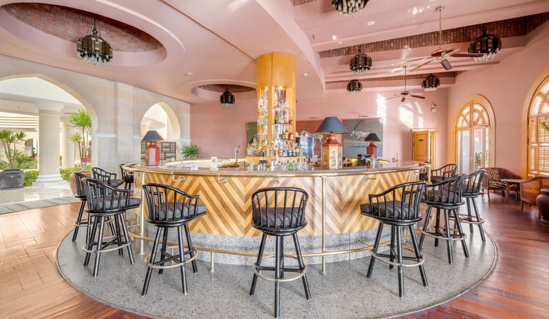 Safari circular cocktail bar with black barstools, pink walls, and a warm wooden floor at Royal Savoy Sharm El Sheikh by Kenwood Travel