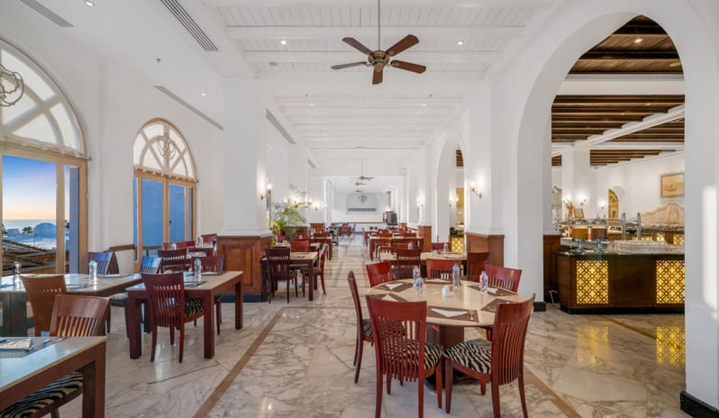 Tirana dining room with white arched ceilings, marble flooring, wooden tables, and a view of the ocean at sunset at Royal Savoy Sharm El Sheikh by Kenwood Travel