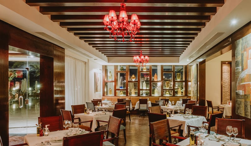 Bella Vista Restaurant white tablecloth tables, wooden chairs, and red crystal chandeliers at Baron Resort Sharm El Sheikh by Kenwood Travel