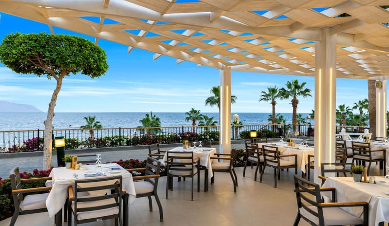 Adalar oceanfront outdoor dining patio with white tablecloth settings under a modern wooden pergola structure at Royal Savoy Sharm El Sheikh by Kenwood Travel