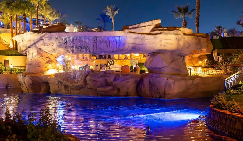 Cave Bar Nighttime view of a swim-up grotto bar with neon blue pool lights and waterfall features at Royal Savoy Sharm El Sheikh by Kenwood Travel
