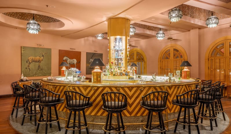 Safari circular cocktail bar with black barstools, pink walls, and a warm wooden floor at Royal Savoy Sharm El Sheikh by Kenwood Travel