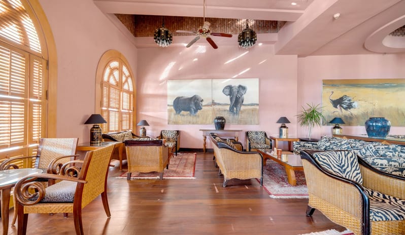 Safari indoor hotel seating area with pink walls, wooden floors, wicker furniture, and large paintings of African wildlife at Royal Savoy Sharm El Sheikh by Kenwood Travel