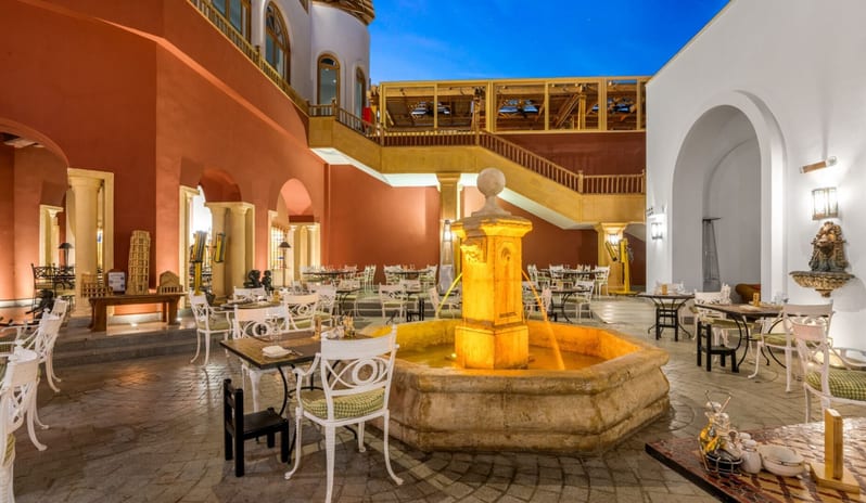 Rosmarino spacious hotel outdoor patio set up for evening fine dining, highlighted by a lit decorative fountain and warm architectural lighting at Royal Savoy Sharm El Sheikh by Kenwood Travel