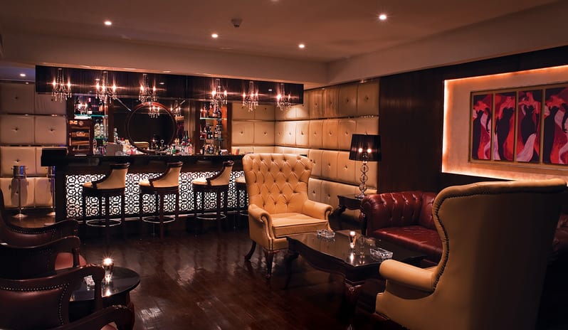 The Niche Bar tufted leather armchairs, a polished wooden floor, and an elegant bar counter with chandeliers at Baron Resort Sharm El Sheikh by Kenwood Travel
