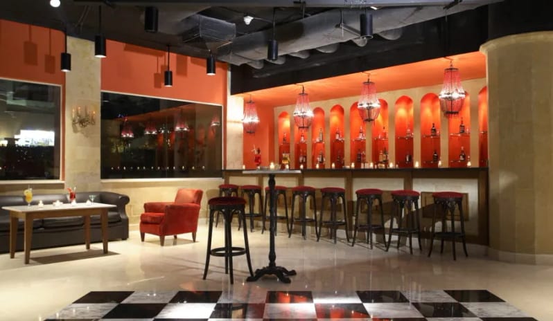 Now & Zen Dance Bar black and white checkered dance floor, high bar stools, and an orange accent wall with illuminated arched liquor shelving at Baron Resort Sharm El Sheikh by Kenwood Travel
