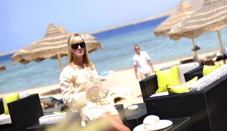 Palm Beach Bar beachfront lounge chairs and thatched umbrellas with guests relaxing by the sea at a luxury resort at Baron Resort Sharm El Sheikh by Kenwood Travel