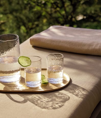 Double Room Ground Floor Sea View close-up shot of a textured glass pitcher and a matching glass, both filled with ice, water, and fresh lime slices on an outdoor table at Sani Club by Kenwood Travel