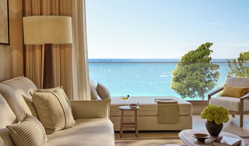 Junior Suite Grand Balcony Sea View balcony with a comfortable daybed lounge, small wooden side table with a cocktail, and a clear glass railing showing a panoramic Mediterranean sea view at Sani Club by Kenwood Travel