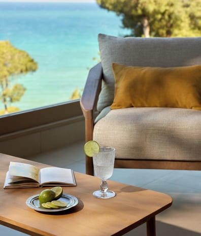 Junior Suite Grand Balcony Sea View Scenic hotel balcony lounge setup with a cozy armchair, summer drink, and panoramic ocean views at Sani Club by Kenwood Travel