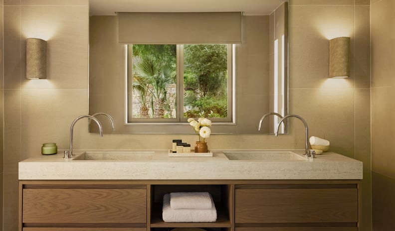 Family Suite Grand Balcony Sea View Luxury bathroom double vanity with integrated stone sinks, modern chrome gooseneck faucets, a large mirror reflecting a garden window, and textured wall sconces at Sani Club by Kenwood Travel