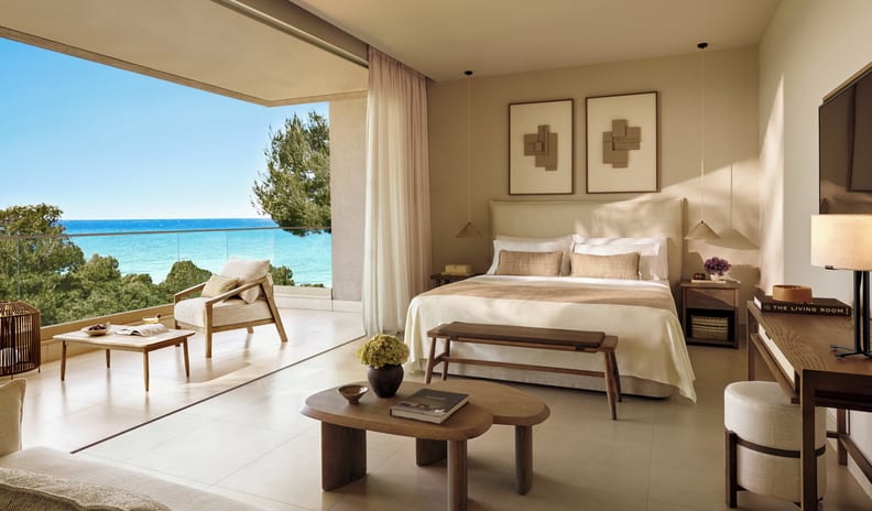 Family Suite Grand Balcony Sea View Luxury hotel bedroom with a minimalist Japandi design, featuring a large balcony overlooking a turquoise ocean, a king-size bed with neutral linens, and organic wooden furniture. at Sani Club by Kenwood Travel